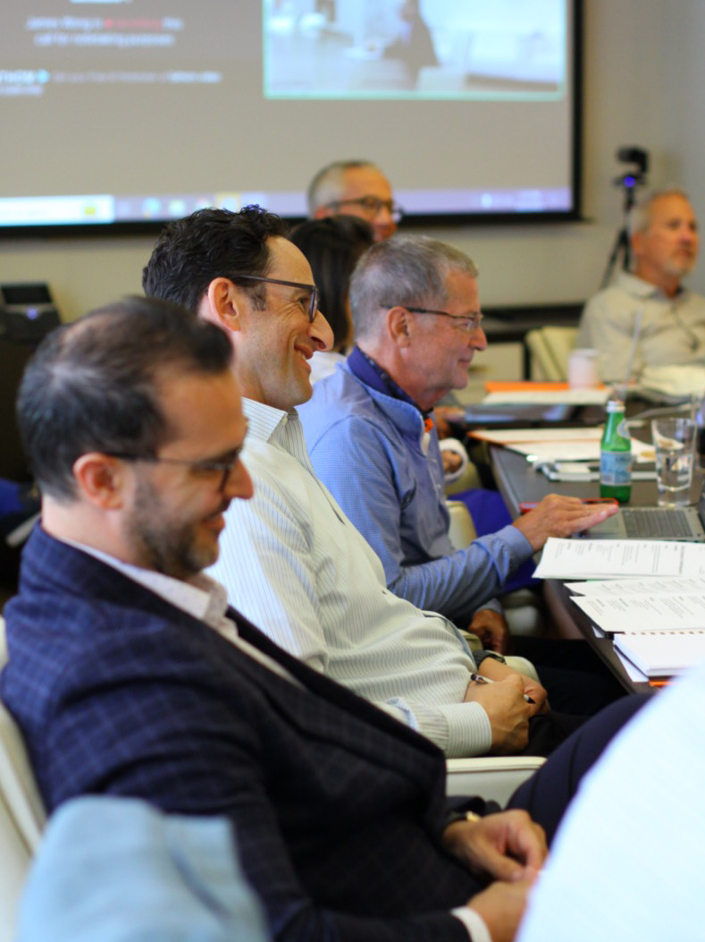 Men sitting at a conference table smiling, watching presentation